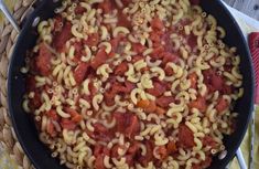 a skillet filled with pasta and sauce on top of a table next to utensils