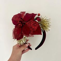 a hand holding a red flower on top of a headband