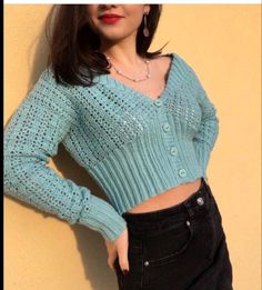 a woman wearing a blue sweater leaning against a wall with her hands on her hips