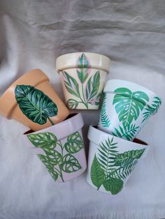 four ceramic plant pots with green leaves painted on the tops and bottom, sitting on a white sheet