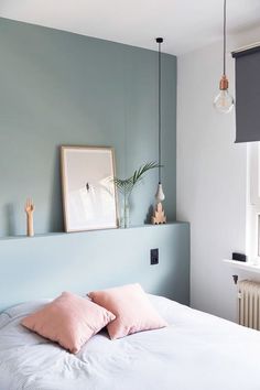 a bed with two pink pillows on top of it next to a wall mounted plant