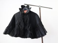 "Antique French black silk cape. Such a great shape with a high collar and wide lace trim. Main fabric is a wide ribbed silk. Fully lined. Closes with a metal hook and eye at the neck.  Measures: 15\" collar, 20 1/4\" long Great condition overall. One piece of broken lace as shown. Some light surface wear mainly to the collar. Edges of the collar are a little worn and frayed too.  Feel free to ask any questions. Ships internationally via signed for delivery." Fitted Gothic Cape For Costume, Formal Black Capelet, Black Capelet For Costume, Elegant Black Cape For Costume, Black Fitted Capelet, Fitted Black Capelet, Elegant Black Capelet For Costume, Costume Capes, Silk Cape