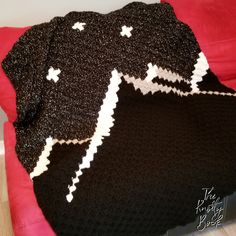 a black and white knitted blanket laying on top of a red bed coverlet