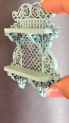 a hand holding a miniature metal shelf with ornate designs on the top and bottom part