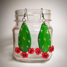 a pair of green earrings with red roses on them sitting in a glass jar filled with water