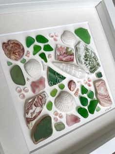 a white frame with sea glass and shells on it's sides, in the shape of a heart