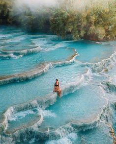 a woman standing in the middle of a river with blue water and steam rising from it