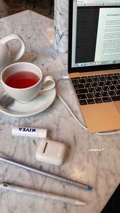 an open laptop computer sitting on top of a marble table next to a cup of tea