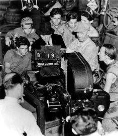 black and white photograph of men working on an old typewriter in a room full of other people