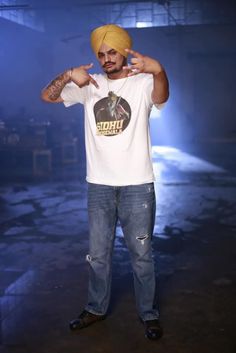 a man with a turban pointing to the side while wearing jeans and a t - shirt