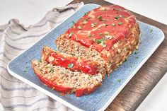 sliced meatloaf with sauce and herbs on a blue plate next to a napkin