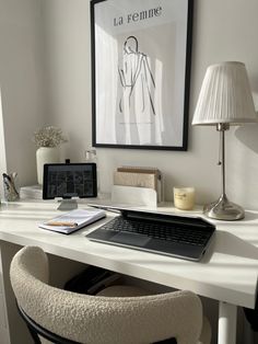 a desk with a laptop, lamp and pictures on the wall in front of it