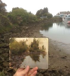 a hand holding an open book in front of a body of water