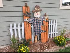 a scarecrow is standing in front of a fence with flowers and plants around it