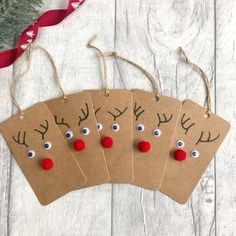 four brown tags with reindeer noses and red noseballs hanging from twine on white wooden background