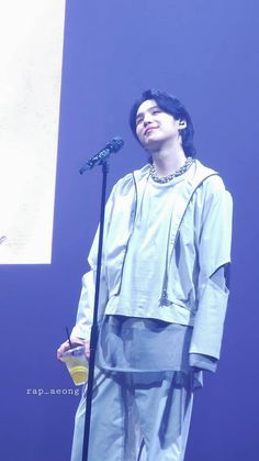 a man standing next to a microphone in front of a blue wall with writing on it