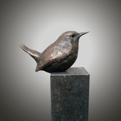 a bronze bird sitting on top of a black block