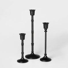 three black candlesticks sitting next to each other on a white surface with one candle in the middle