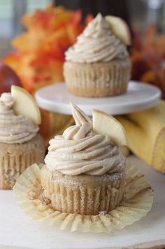 three cupcakes with frosting and apples in the background