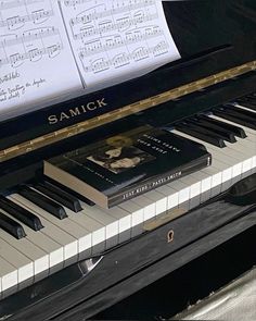 a black piano with sheet music on it's keys and the words samick written in gold