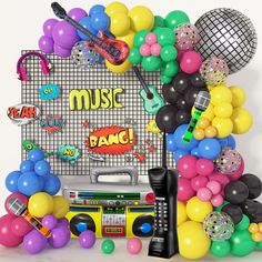 an assortment of balloons, music equipment and streamers in front of a white backdrop