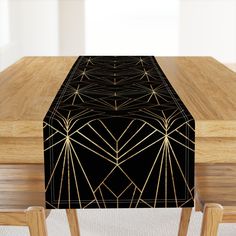 a wooden table topped with a black and gold table runner covered in art deco design