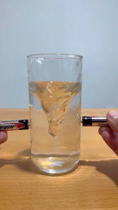 two hands holding an electronic device near a glass with liquid in it on a wooden table