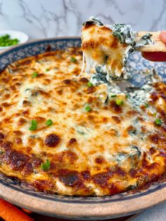 a hand holding a piece of pizza with cheese and spinach on it in a bowl