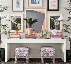 a white table topped with lots of pictures and plants next to two pink stools