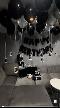 a living room filled with lots of black and white balloons hanging from the ceiling next to a couch