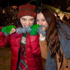 two girls are posing for the camera with christmas decorations on their hands and one girl is wearing a red jacket