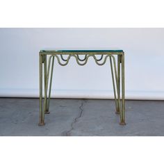 a green table sitting on top of a cement floor next to a white wall with an iron frame