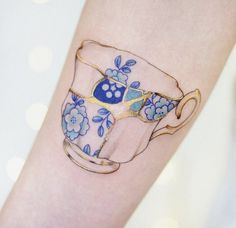 a tattoo on the arm of a woman with a blue and white teacup in it