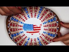 someone is painting an american flag on a plate with red, white and blue beads