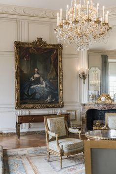 a living room filled with furniture and a chandelier hanging from the ceiling next to a painting