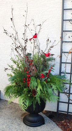 a black vase filled with red berries and greenery on top of a sidewalk next to a white wall