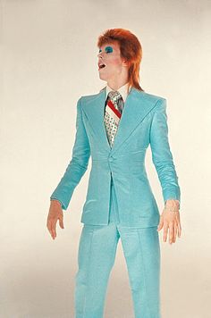 a man in a blue suit and tie with his hands on his hips, standing