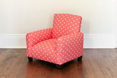 a red chair sitting on top of a hard wood floor next to a white wall