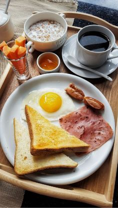 a breakfast plate with eggs, ham, toast and coffee on a wooden serving tray