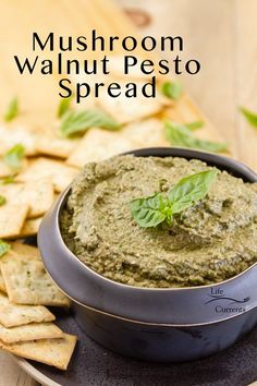 a bowl filled with green pesto next to crackers on a wooden table and text overlay that reads mushroom walnut pesto spread