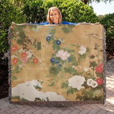 a woman holding up a large tapestry with flowers on it's side and smiling at the camera