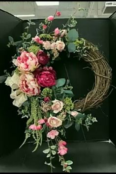 a wreath with pink flowers and greenery hanging from the front of a black wall