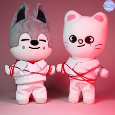 two stuffed animals are standing next to each other on a pink background, one is wearing a white outfit and the other has a red ribbon around its neck