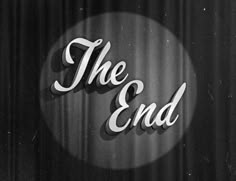 black and white photo of the end sign on a curtained stage with light coming from behind it