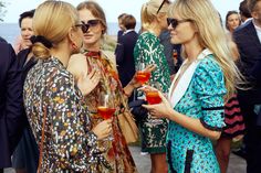 two women standing next to each other with drinks in their hands and people looking at them