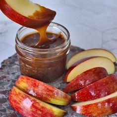 an apple slice being dipped with caramel on top of some apples and peanut butter