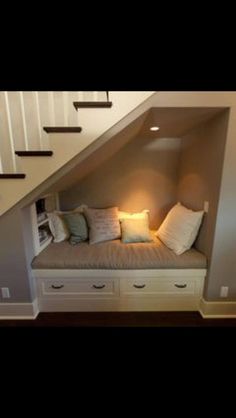 a room that has some drawers under the stairs and a bench with pillows on it