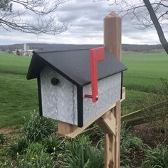 a mailbox in the shape of a house on a wooden post with grass and trees behind it