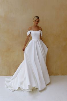 a woman in a white wedding dress standing against a wall with her hands on her hips