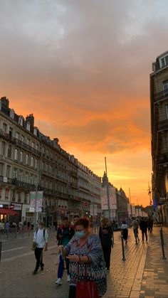 people are walking on the sidewalk in front of some buildings at sunset or sunrise time